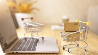 Online shopping and delivery service concept.Brown paper boxs in a shopping cart with laptop keyboard on wood table in office background.Easy shopping with finger tips for consumers.